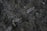 Close-up view of dark soil with small rocks and organic matter, featuring a mix of rough textures and varying shades of brown and dark gray.