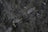 Close-up view of dark soil with small rocks and organic matter, featuring a mix of rough textures and varying shades of brown and dark gray.