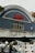 A classic cinema facade features an arched roof with a neon sign spelling 'Electric Cinema' in cursive red letters. The building's exterior is adorned with intricate floral carvings and has a vintage architectural style. In the foreground, out-of-focus decorative bulbs hang, adding a cozy ambiance, while a street vendor's stand and some parts of vehicles are partially visible.