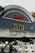 A classic cinema facade features an arched roof with a neon sign spelling 'Electric Cinema' in cursive red letters. The building's exterior is adorned with intricate floral carvings and has a vintage architectural style. In the foreground, out-of-focus decorative bulbs hang, adding a cozy ambiance, while a street vendor's stand and some parts of vehicles are partially visible.