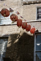 A row of traditional red lanterns strung across a brick facade, casting shadows on the wall. Small Union Jack flags hang alongside the lanterns. The building features multiple windows with white frames, reflecting some light.