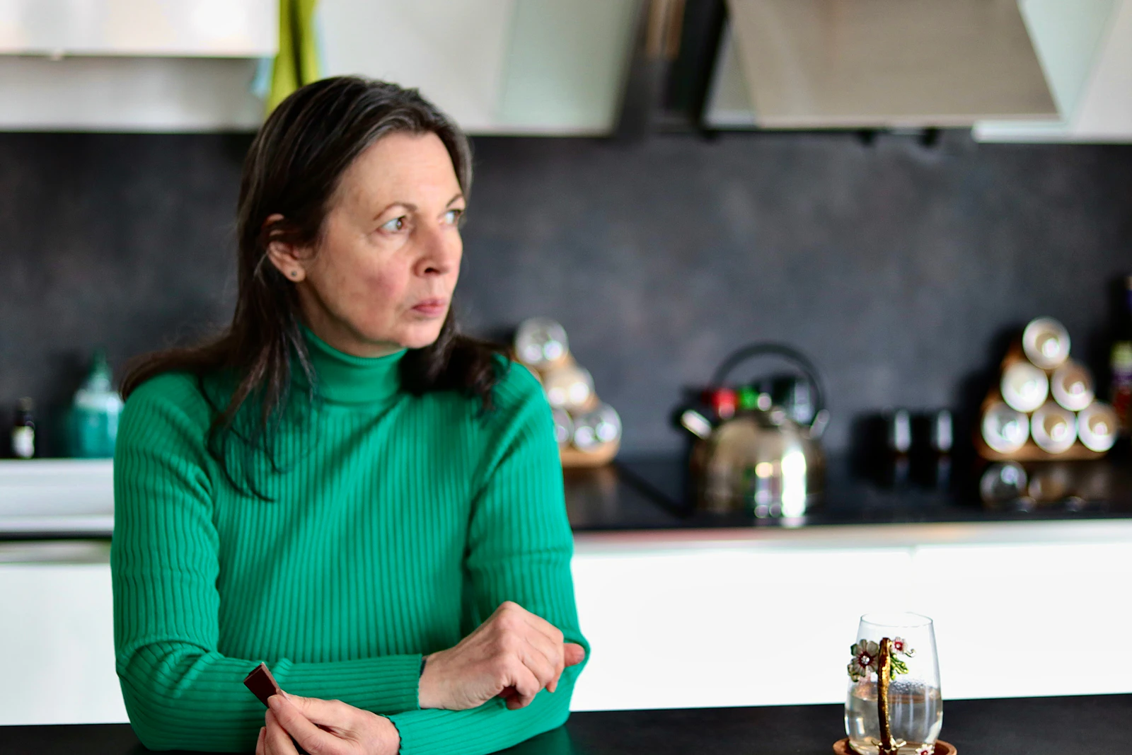 A woman sitting alone at a kitchen table in natural light, looking worried, after being told her test results were normal