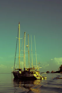 Vintage wooden sailing ship anchored near Nevis shore, bathed in golden afternoon light.