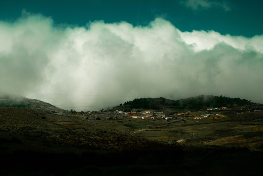 a hill covered in clouds and a small town in the distance