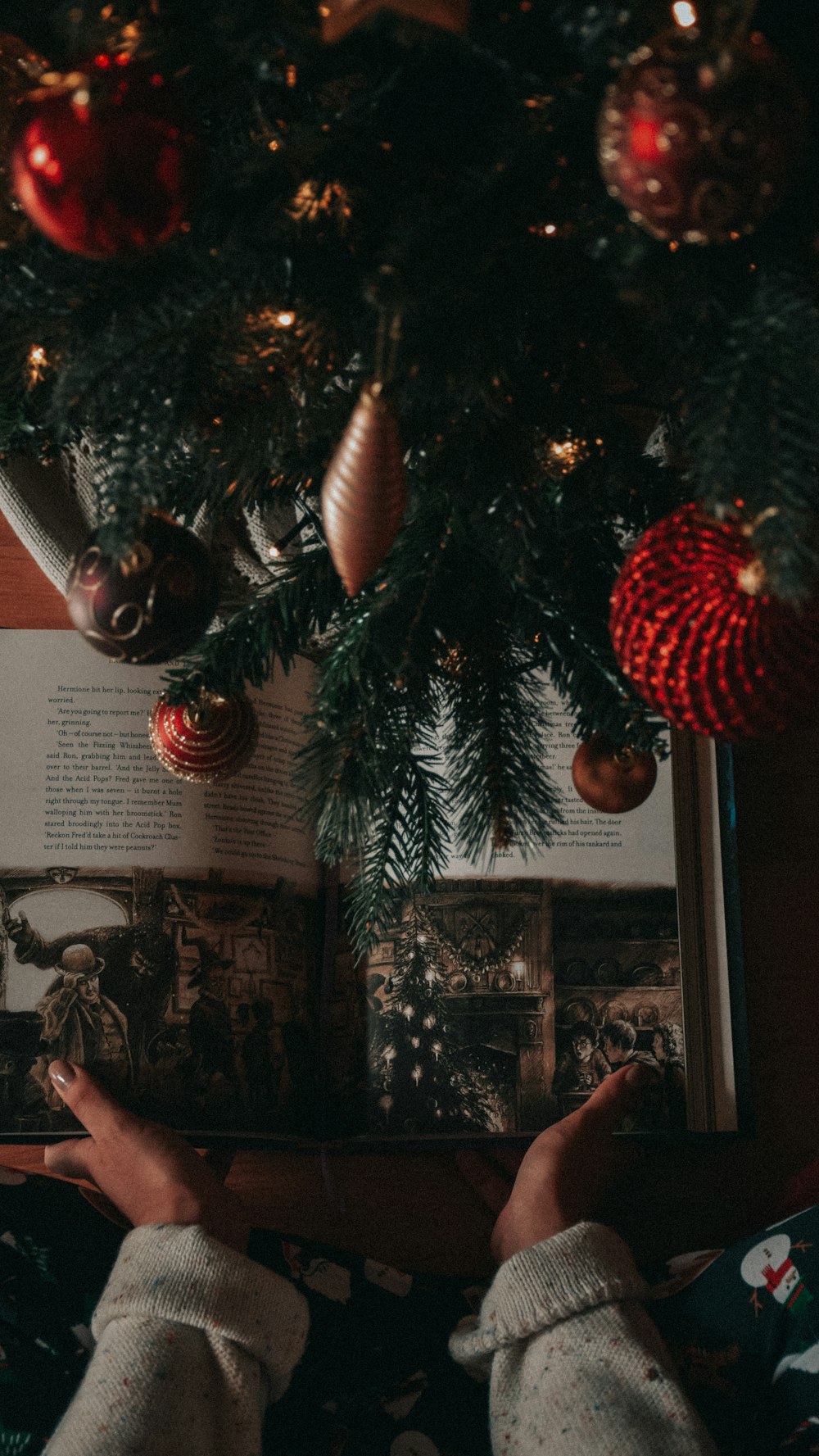 a person reading a book under a christmas tree