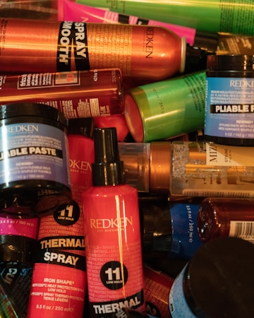 A collection of various hair styling products from the brand Redken, including thermal sprays, pliable paste, and other haircare items in a variety of colorful packaging such as red, orange, blue, and green bottles and jars.