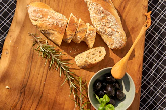 Rustic loaf of freshly baked Genovese focaccia resting on a wooden board with olive oil and herbs.