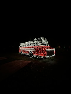 A bus is outlined in lights against a dark background. The bus is decorated with numerous small white and red lights, giving it a festive appearance.