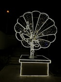A large, intricately designed structure resembling an old-fashioned gramophone, illuminated against a dark background. The gramophone features musical notes and a glowing outline, creating a striking visual effect.