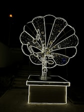 A large, intricately designed structure resembling an old-fashioned gramophone, illuminated against a dark background. The gramophone features musical notes and a glowing outline, creating a striking visual effect.