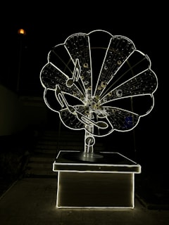 A large, intricately designed structure resembling an old-fashioned gramophone, illuminated against a dark background. The gramophone features musical notes and a glowing outline, creating a striking visual effect.