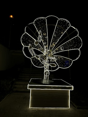 A large, intricately designed structure resembling an old-fashioned gramophone, illuminated against a dark background. The gramophone features musical notes and a glowing outline, creating a striking visual effect.