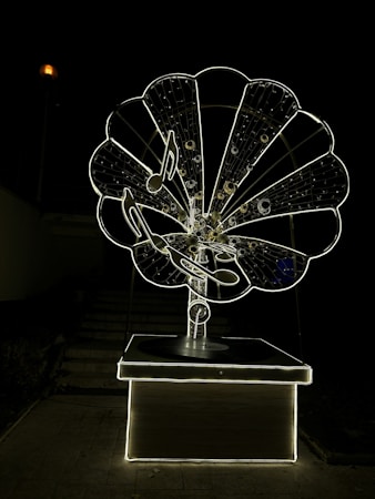 A large, intricately designed structure resembling an old-fashioned gramophone, illuminated against a dark background. The gramophone features musical notes and a glowing outline, creating a striking visual effect.