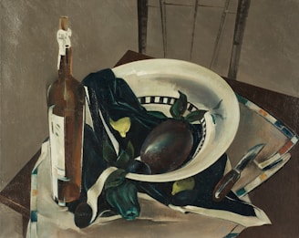 A still life painting featuring a white bowl with a decorative pattern along the edge, containing a dark-colored fruit and leaves. There is a dark cloth draped inside the bowl and partially over the table. A wine bottle with a white label is positioned to the left of the bowl. To the right, a knife is placed on the table beside a white napkin with striped edges. The background includes a part of a chair and a plain wall.