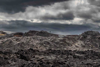 A lone figure standing on a cracked earth landscape under a glowing, ominous sky filled with distant stars.