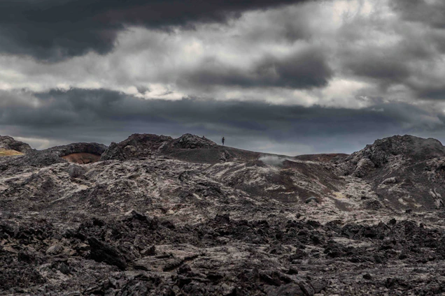 A lone figure standing on a cracked earth landscape under a glowing, ominous sky filled with distant stars.