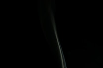 A dark background with a subtle, elongated wisp of smoke or vapor winding upward, casting a mysterious and elegant aura. The form is smooth and slightly translucent.
