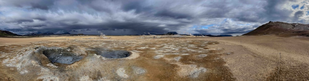 a dirt field with a sky filled with clouds