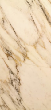 A close-up of a marble surface with swirling patterns of beige, cream, and grey with subtle veins running across.