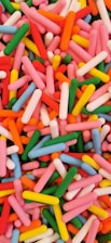 A vibrant assortment of colorful, cylindrical candy pieces scattered randomly. The candy pieces are predominantly pink, red, green, yellow, blue, and orange, creating a lively and playful visual effect.