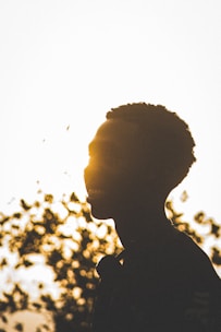 a man standing in front of a tree with the sun behind him