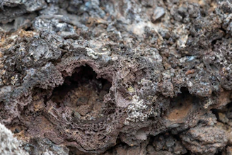 Close-up of a small geopolymetric pot with violet iron oxide texture and volcanic greba black notes, shimmering mica highlights.