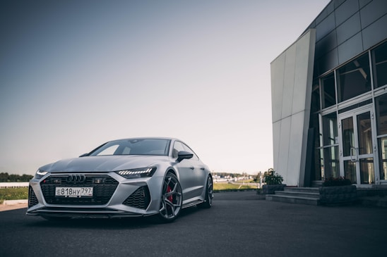 A sleek metallic grey car parked in front of a modern Bavarian dealership building under a clear sky.