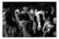 A black and white image featuring people wearing numbered sports jerseys. The focus is on individuals with numbers 28, 5, 11, and 39 visible on their jerseys. Some people have their hands raised and appear to be interacting in a communal or celebratory manner. The background is blurred, indicating others are present but out of focus.