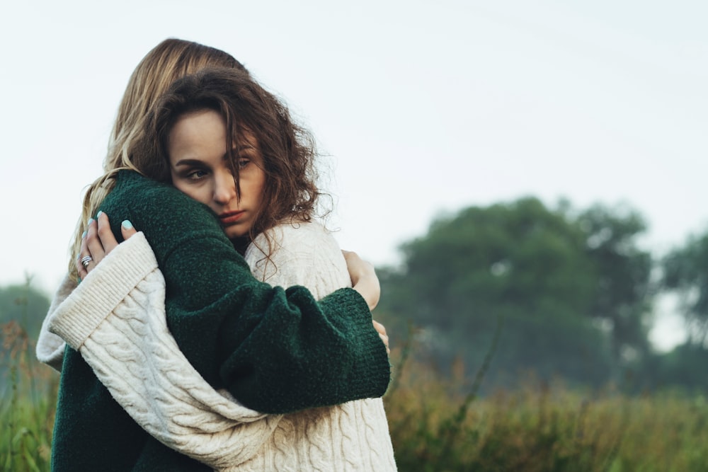 a woman in a green and white sweater hugging a woman in a green and white