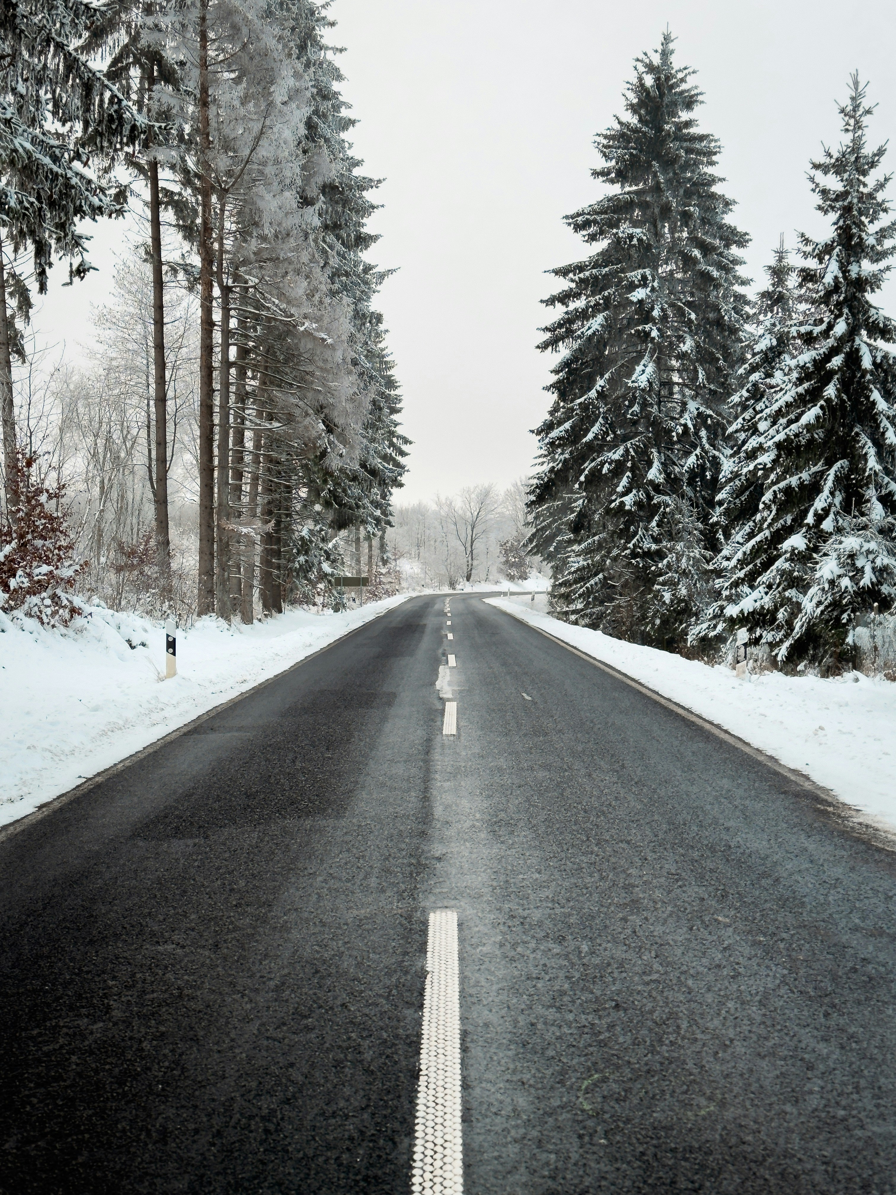 a road with snow on the ground and trees in the background