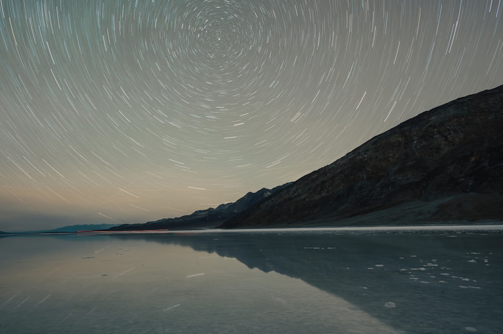a star trail over a lake with mountains in the background