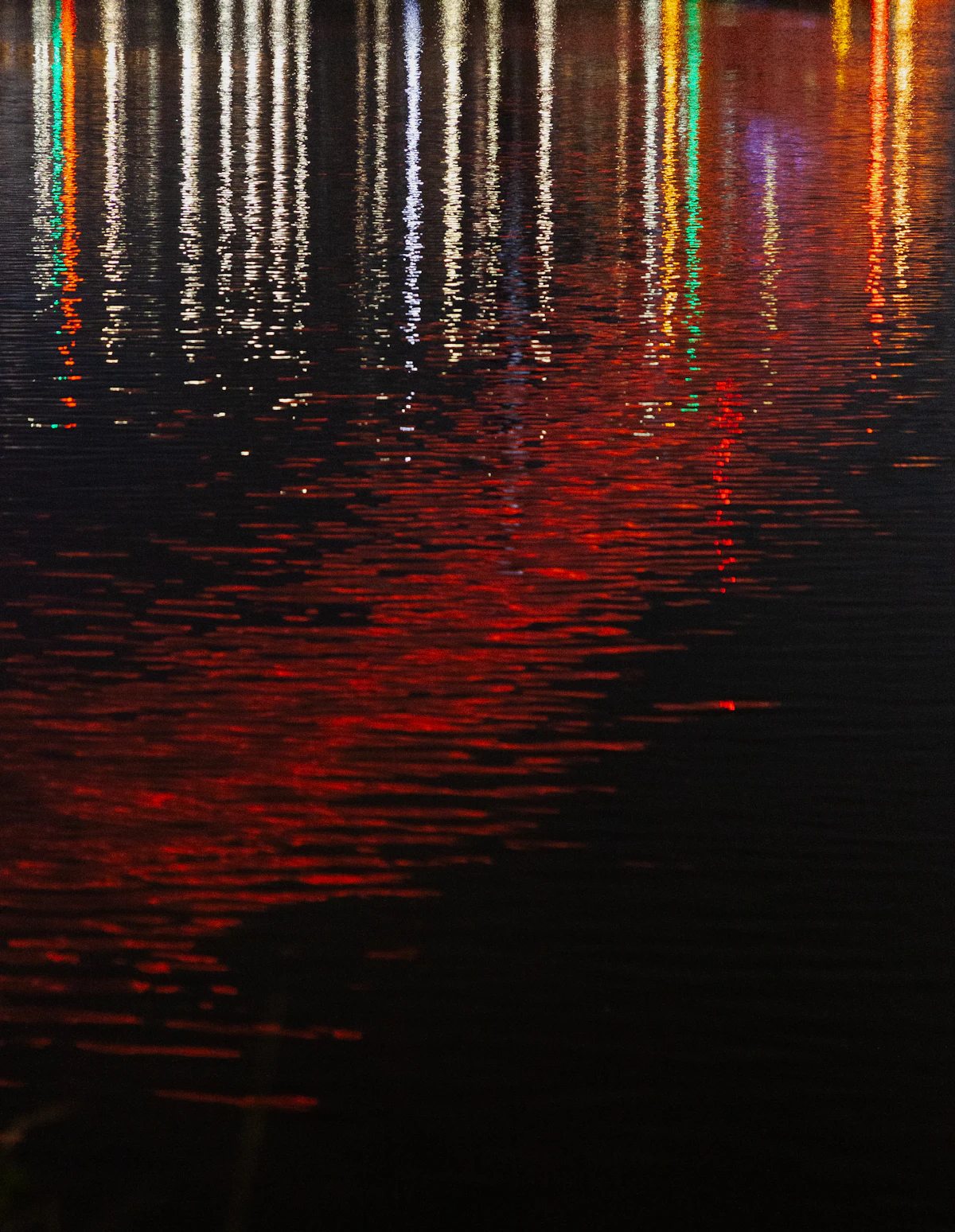 Red and gold festival lights reflected in rippling dark water at night