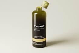 A large, dark green shampoo bottle stands upright with a light-colored cap floating above it. The bottle is labeled with the word 'mockup' in white lettering, and additional smaller text is present below. The background is a gradient of light, neutral tones.