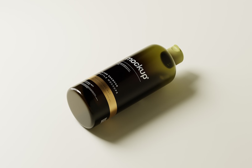 A sleek, dark-colored plastic bottle lying on its side, with the word 'mockup' prominently displayed on its label. The bottle has a cylindrical shape with a gold band near the bottom and a greenish cap on top.