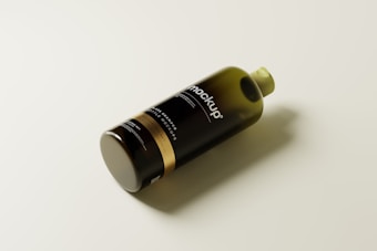 A sleek, dark-colored plastic bottle lying on its side, with the word 'mockup' prominently displayed on its label. The bottle has a cylindrical shape with a gold band near the bottom and a greenish cap on top.