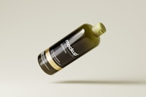 A sleek, dark glass bottle featuring labeled text indicating it is a mockup design. The bottle is tilted and floating against a neutral, light background.