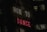 A neon sign with the words 'HOW TO' in white and 'DANCE' in red, set against a dark urban backdrop. Windows of a nearby building are visible in the background.