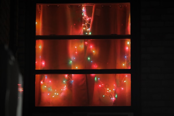 Colorful string lights draped around a festive mantel and window frame.