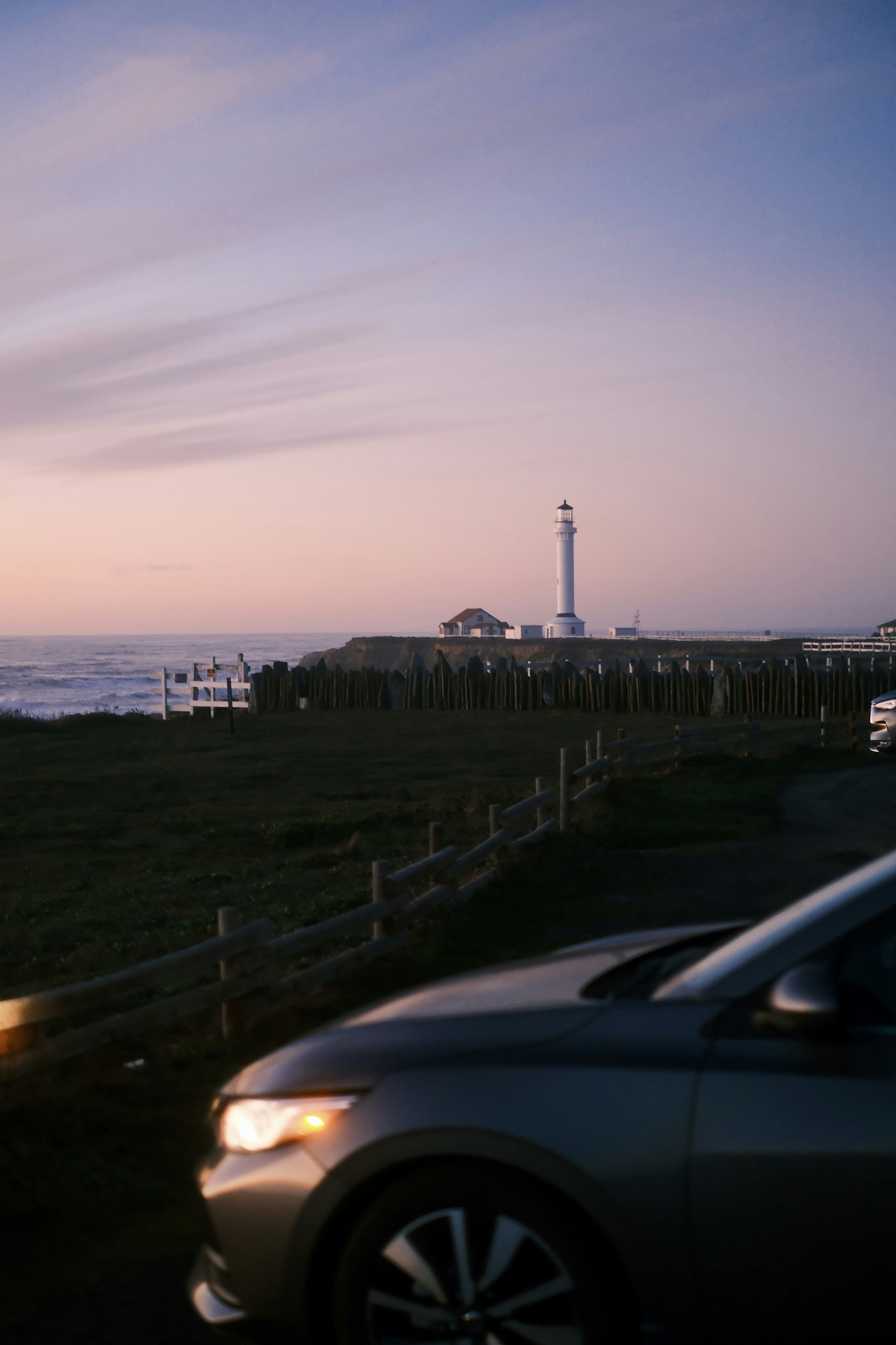 A car parked on the side of a road next to a light house photo – Free ...
