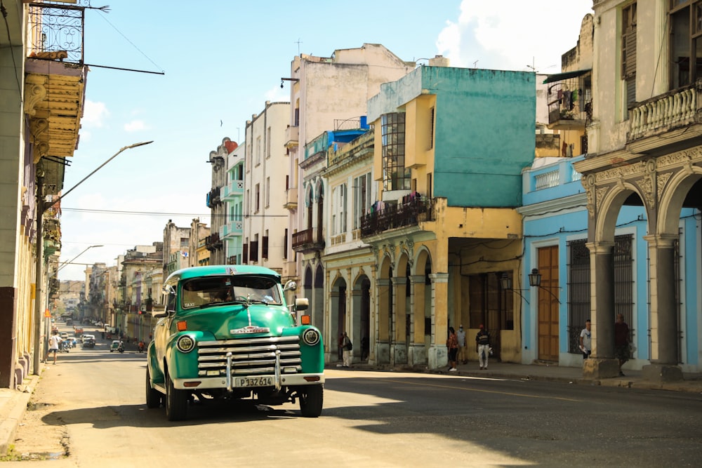 a green truck driving down a street next to tall buildings