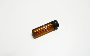 A clean, amber-toned vial filled with hydrobromic acid, set against a dark oxidized red background.