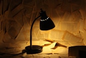 A stack of well-worn books and a glowing desk lamp in a quiet writing nook.