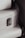 A close-up view of a textured white suitcase with metal hardware, featuring a latch and accentuated by black straps on the sides.