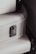 A close-up view of a textured white suitcase with metal hardware, featuring a latch and accentuated by black straps on the sides.