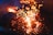 A barbecue grill with glowing charcoal briquettes emits bright, fiery sparks. The grill bars are illuminated by the intense heat of the coals, creating a dynamic scene with orange and yellow flames contrasting against the dark background.