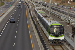 A modern light rail train passing through Seattle with a cityscape backdrop.