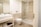 A modern bathroom featuring a glass-enclosed shower area, a wall-mounted toilet, and a sleek rectangular sink on a vanity with storage space underneath. The walls and floor are tiled in a light beige color, and there is a towel and toiletries visible on the vanity shelf.