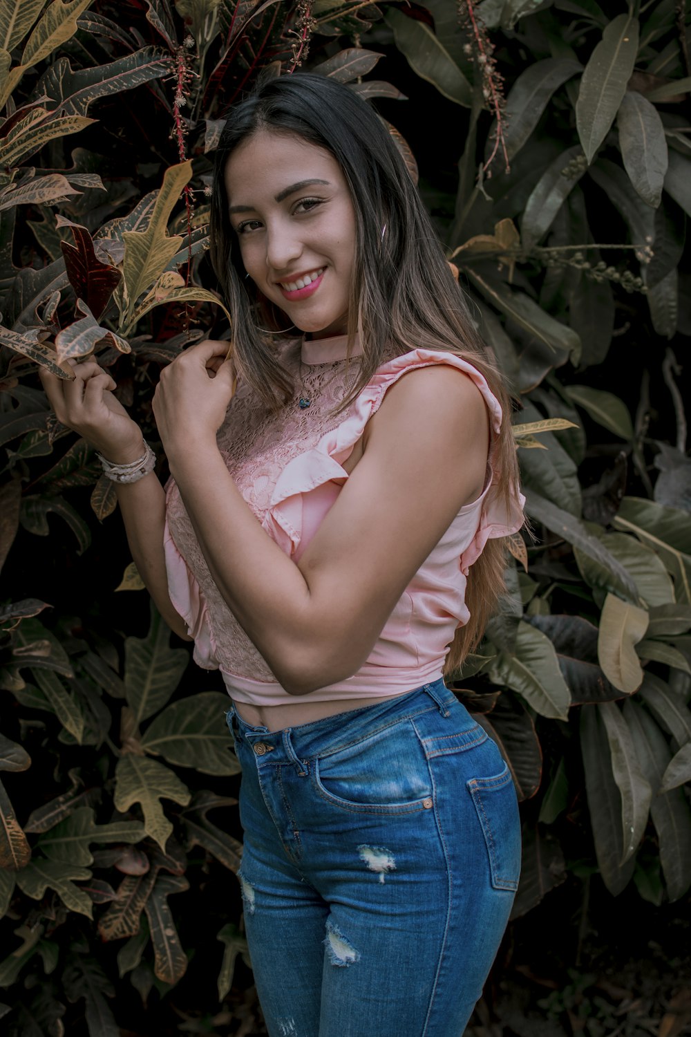 a woman standing in front of a bush holding onto a plant