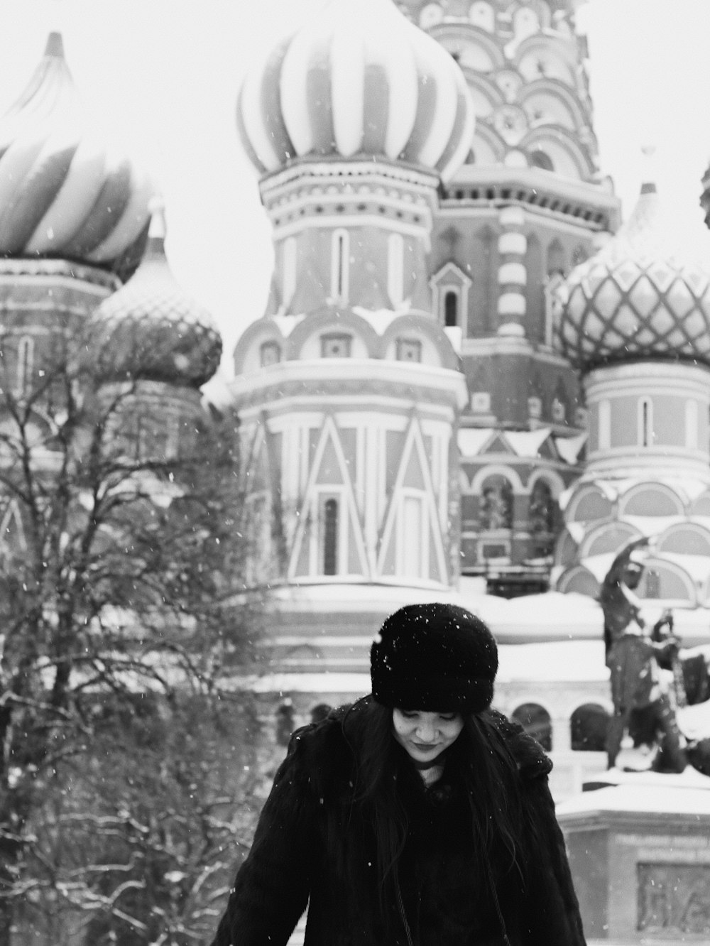 a woman in a black coat and hat walking in the snow