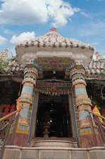 Entrance of Geeta Bhawan Ashram featuring light blue and saffron accents under a clear sky.